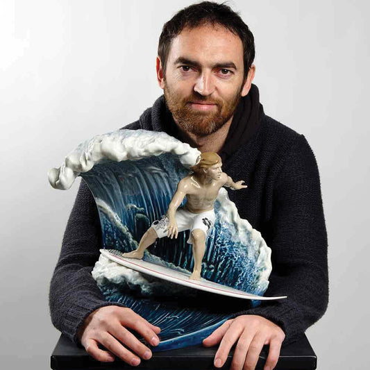 Lladró Sculptor holding a detailed porcelain sculpture of a surfer riding a blue wave