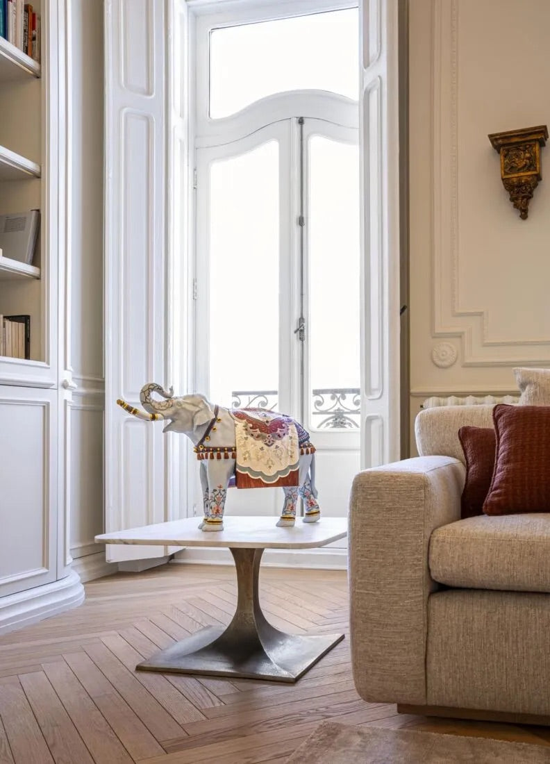 Decorative elephant on a small table in a stylish living room with a sofa and large window.