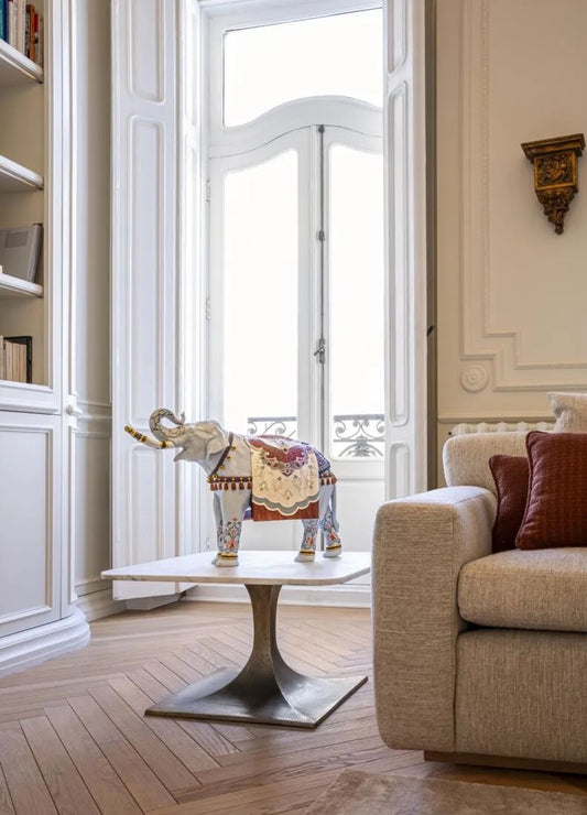 Decorative elephant on a small table in a stylish living room with a sofa and large window.