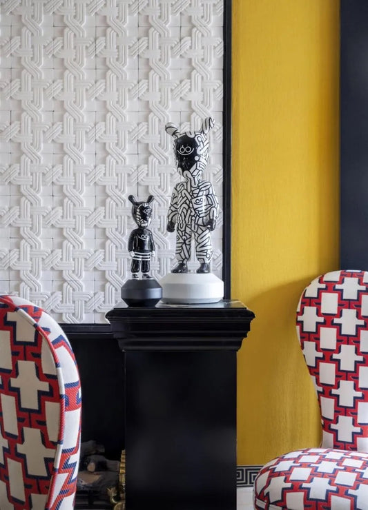 Decorative room with patterned wallpaper, colorful chairs, and decorative items on a black pedestal.