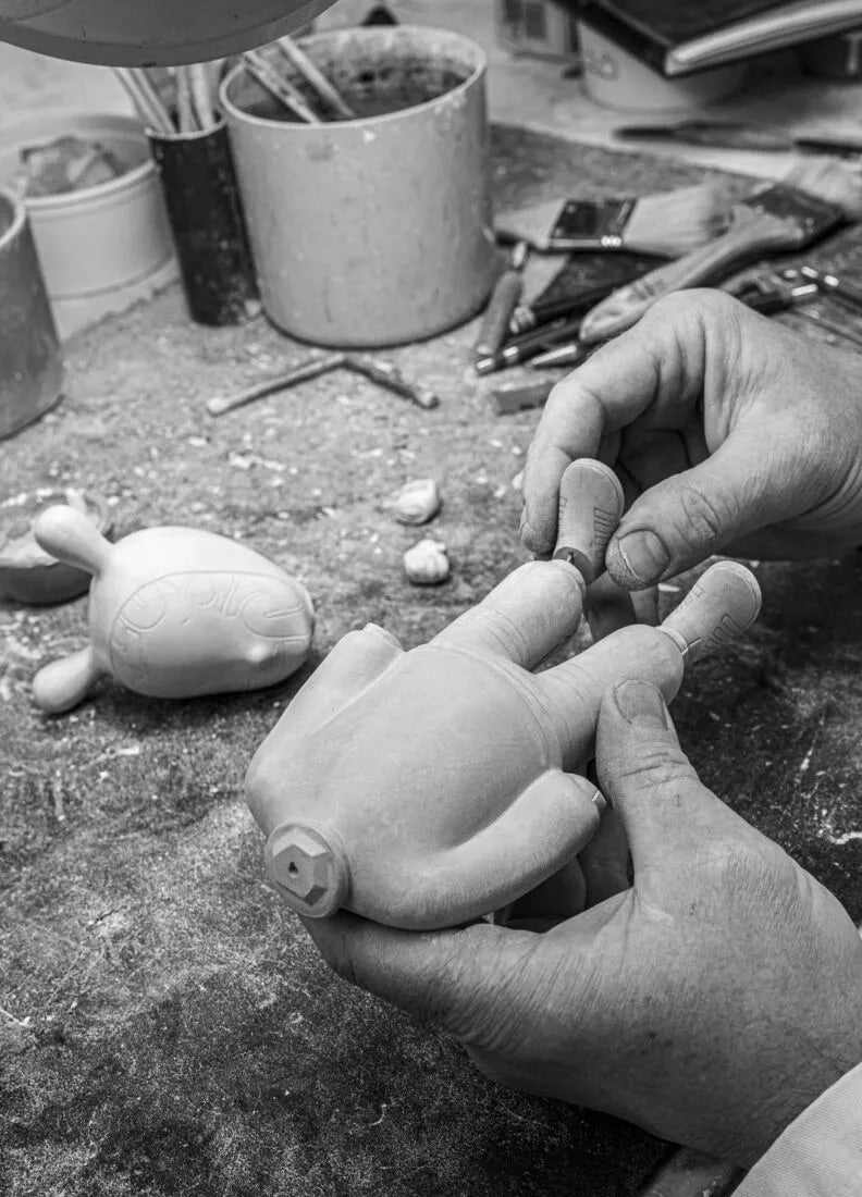 Person working on a ceramic sculpture of a figure with tools and materials in the background.