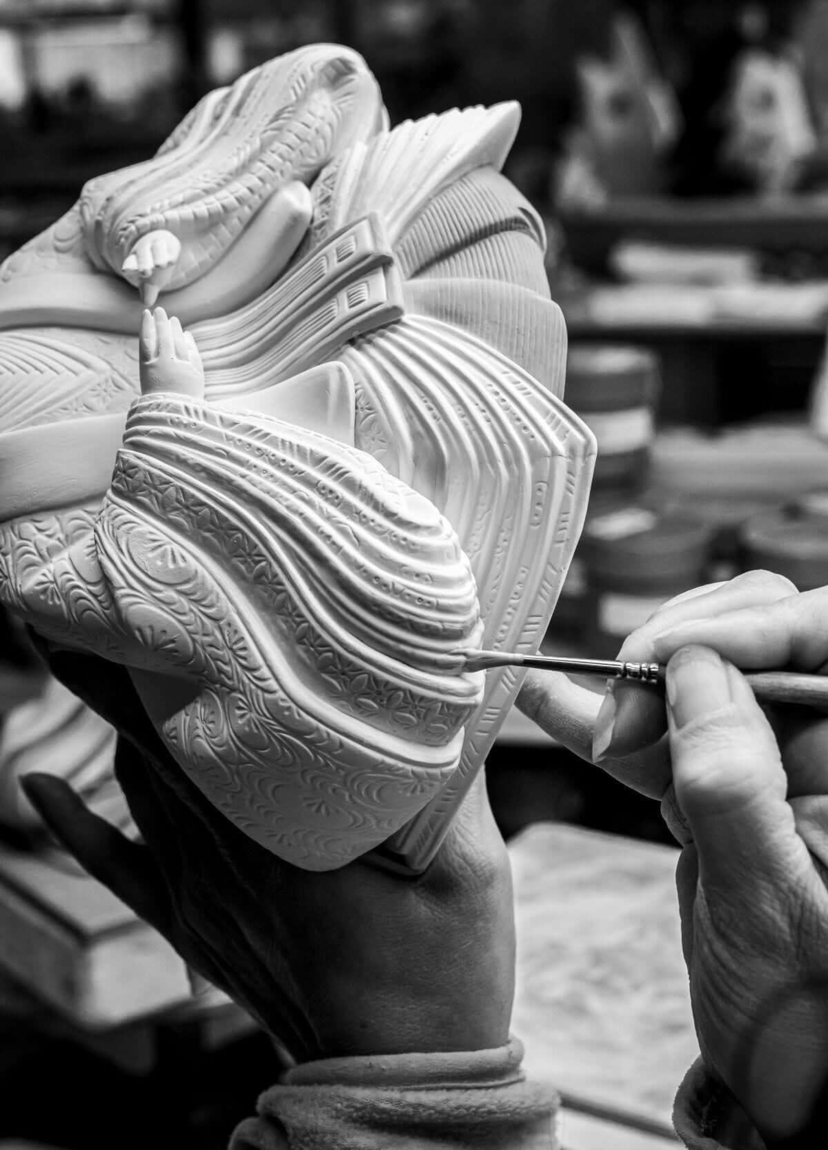 Artisan delicately painting a Hina Doll figurine, showcasing intricate details and craftsmanship in black and white.