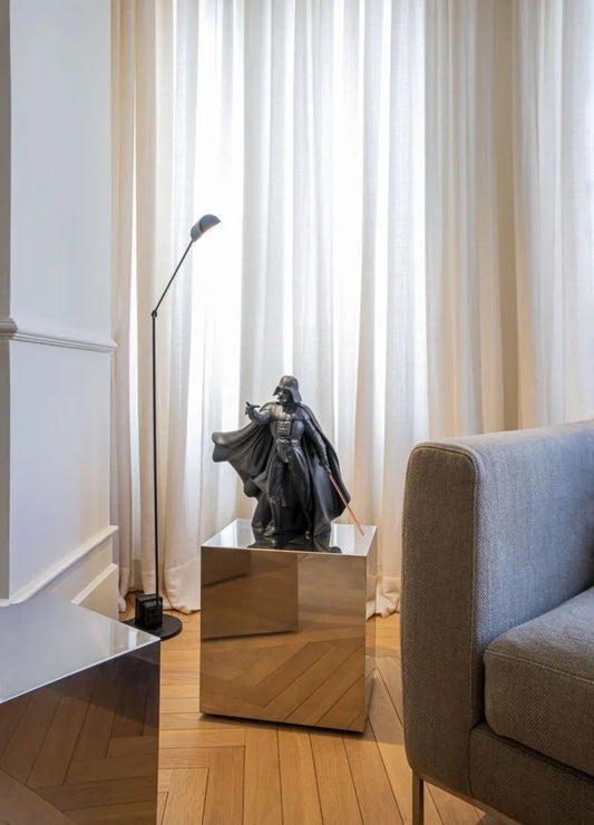 Darth Vader Sculpture on a reflective surface in a room with curtains and a chair.