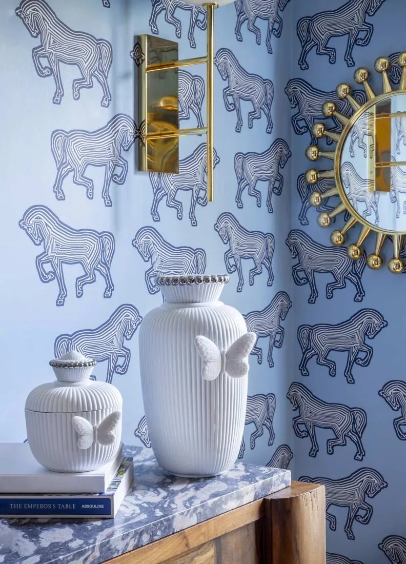 Decorative setting with white vases and books against a blue wall with animal pattern