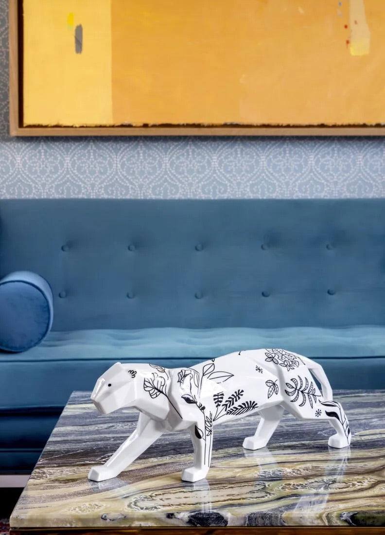 White panther figurine on a wooden table with a blue upholstered chair and patterned wall in the background