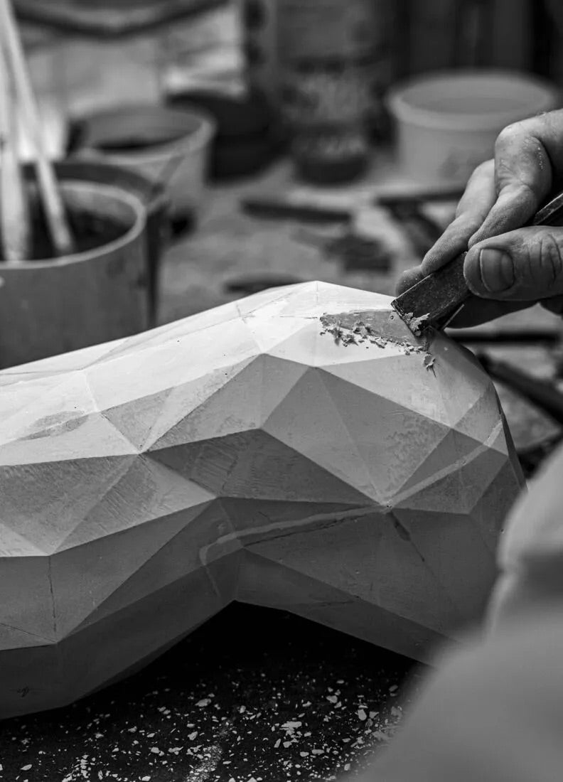 Person working on a geometric porcelain sculpture with tools in a workshop setting.