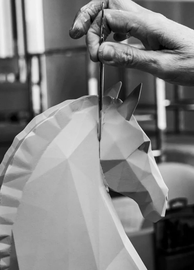 Person cutting a geometric porcelain horse model with scissors.