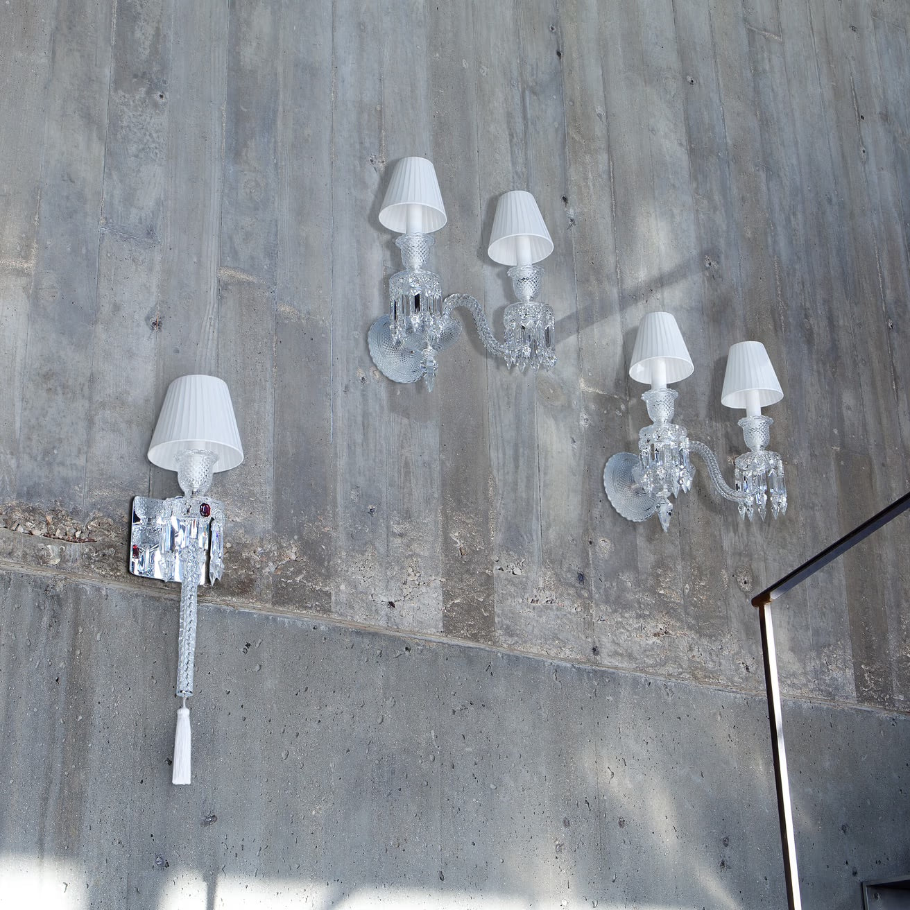 Crystal wall sconces with white lampshades on a concrete wall.