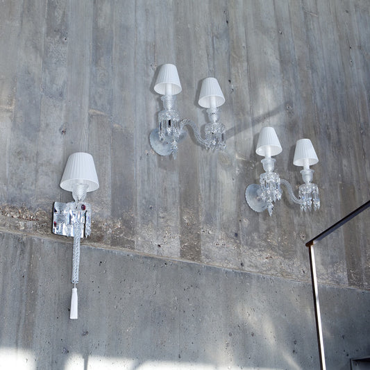 Crystal wall sconces with white lampshades on a concrete wall.