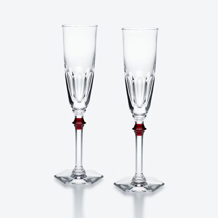 Two clear champagne flutes with red stems on a white background