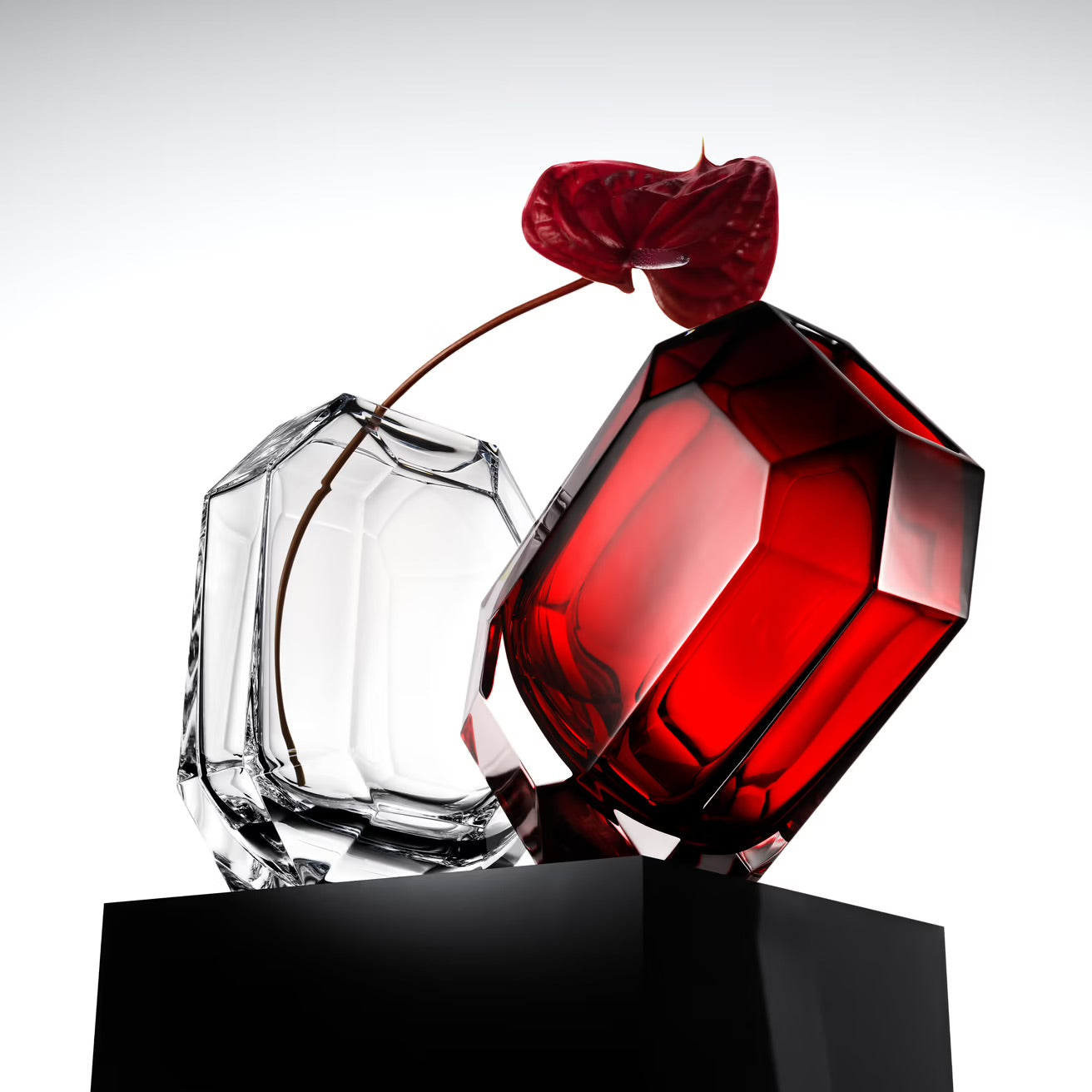 Two faceted perfume bottles, one red and one clear, with a red rose between them on a white background.