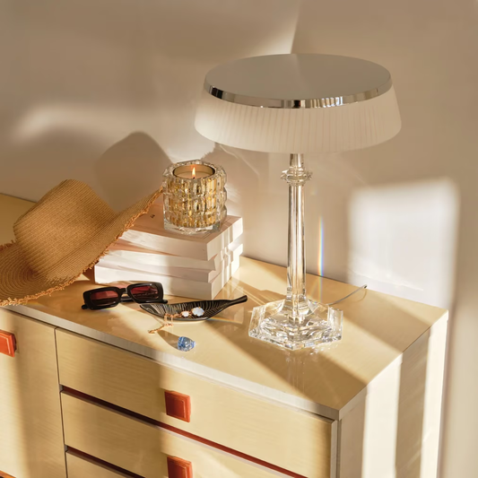 Table with a lamp, books, sunglasses, and a hat on a wooden surface.