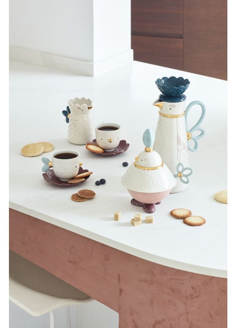 Ceramic tea set with teapot, cups, and cookies on a white surface.