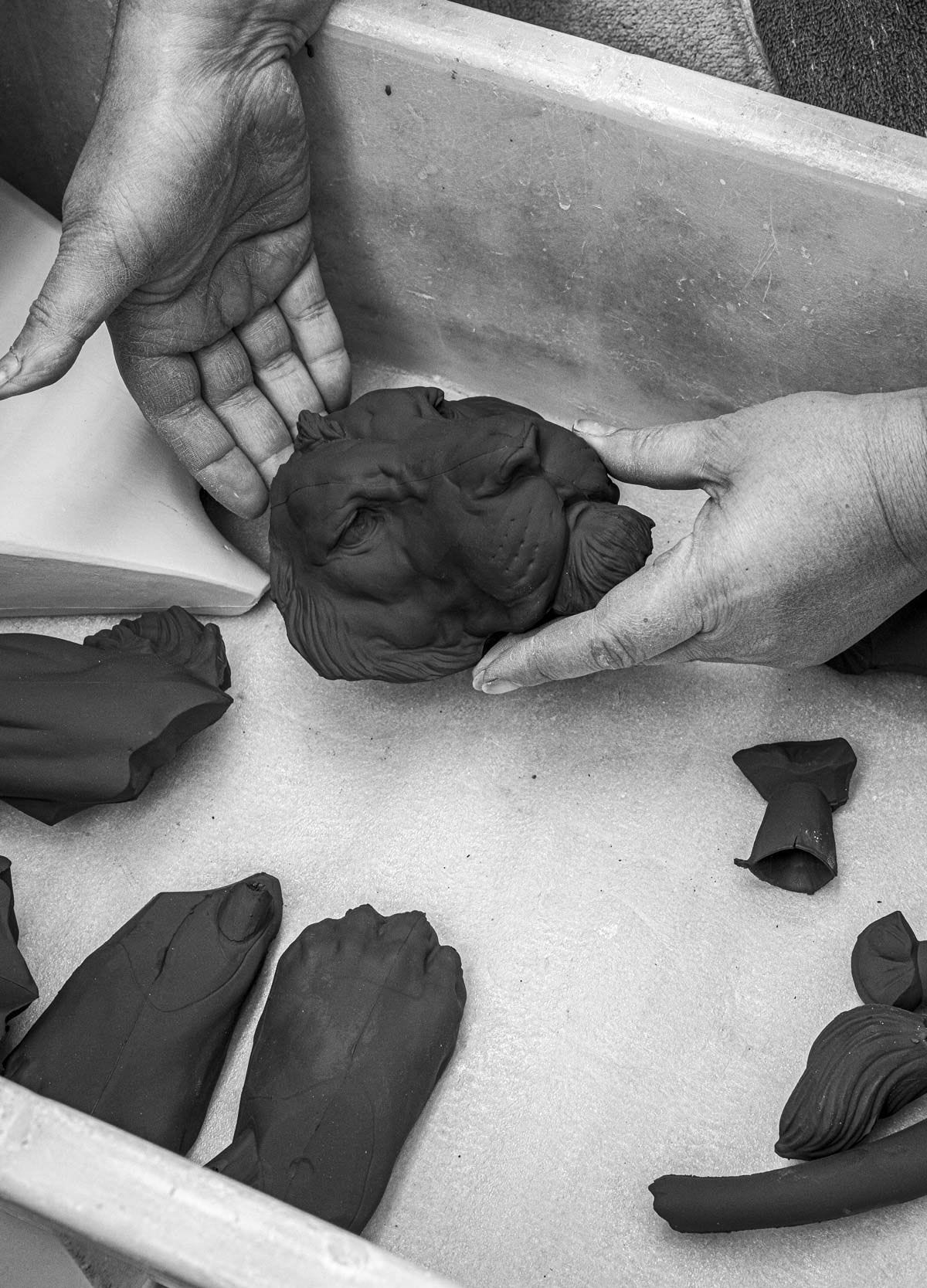 Artisan shaping matt black clay into a lion sculpture, showcasing craftsmanship in black and white.