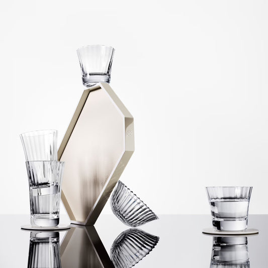 Set of glassware including a carafe and three glasses on a reflective surface with a white background