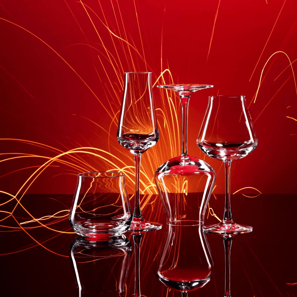 Set of glass wine glasses on a reflective surface with red and orange light streaks in the background.