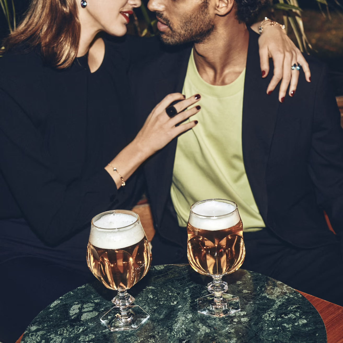 Two people sitting together with two Baccarat glasses of beer on a table.